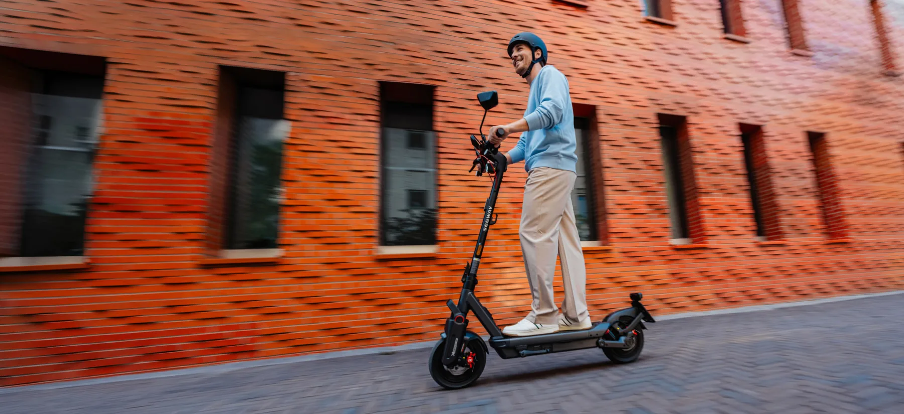 Een man rijdt op een Segway Ninebot MAX G3 NL langs een bakstenen gevel